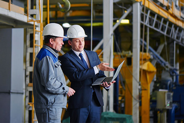 two men in white hard hats looking at a tablet
