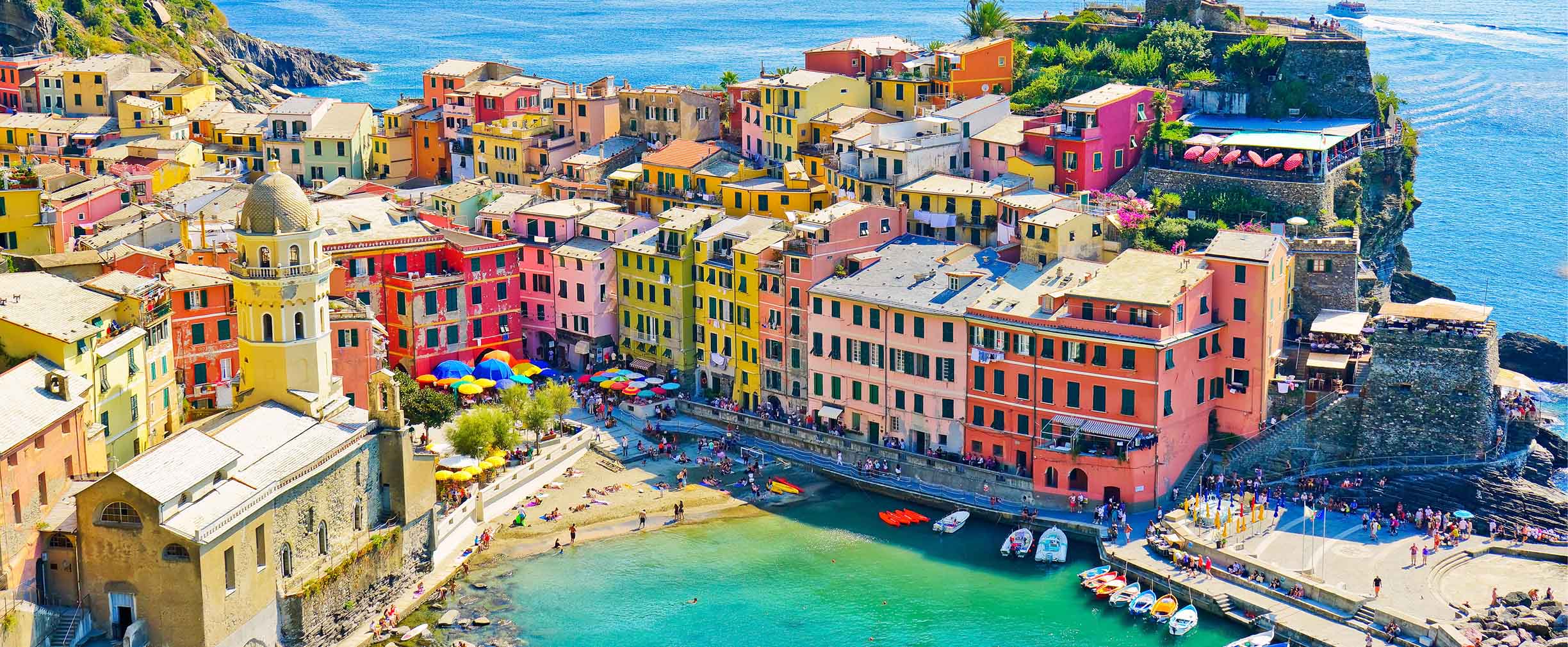 An aerial photo of the Italian seaside town of Cinque Terre complete with colorful houses and a harbor full of quaint fishing boats