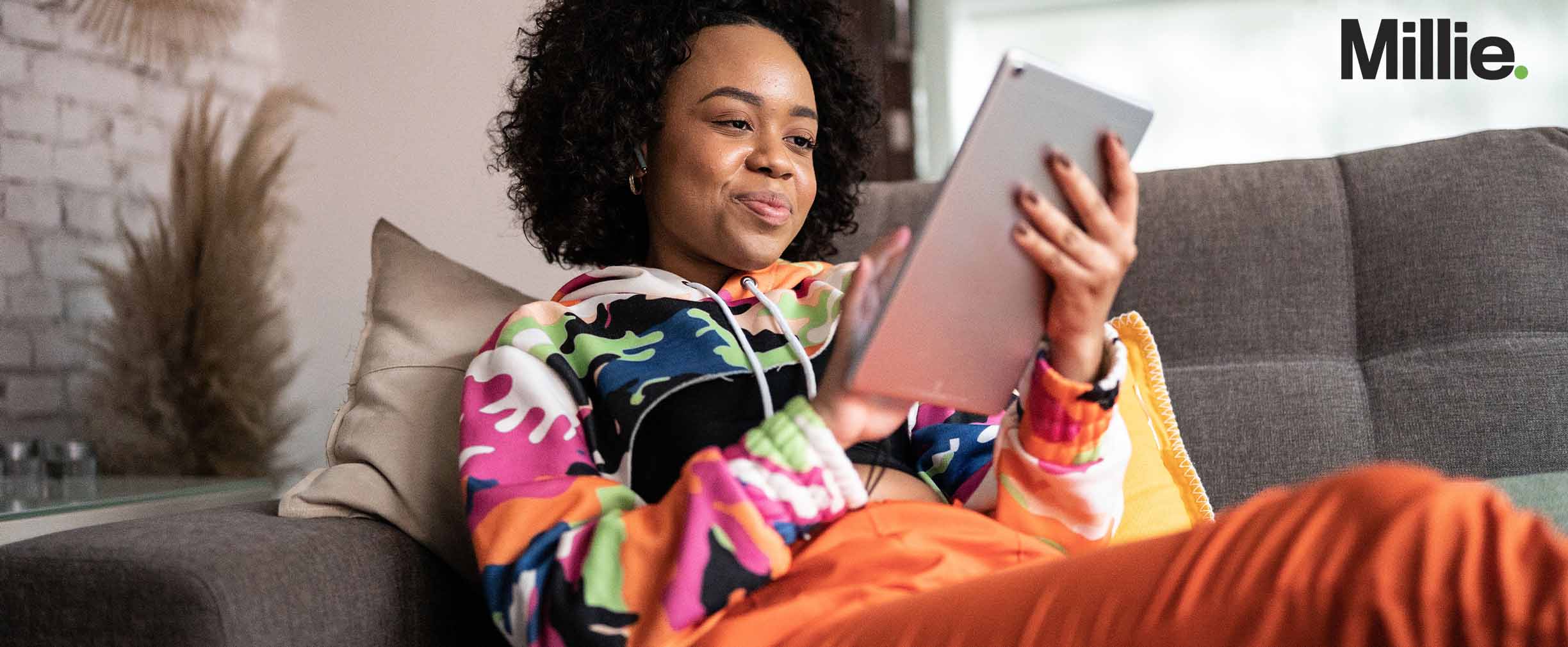 Una joven sentada en un sofá mirando su tableta.