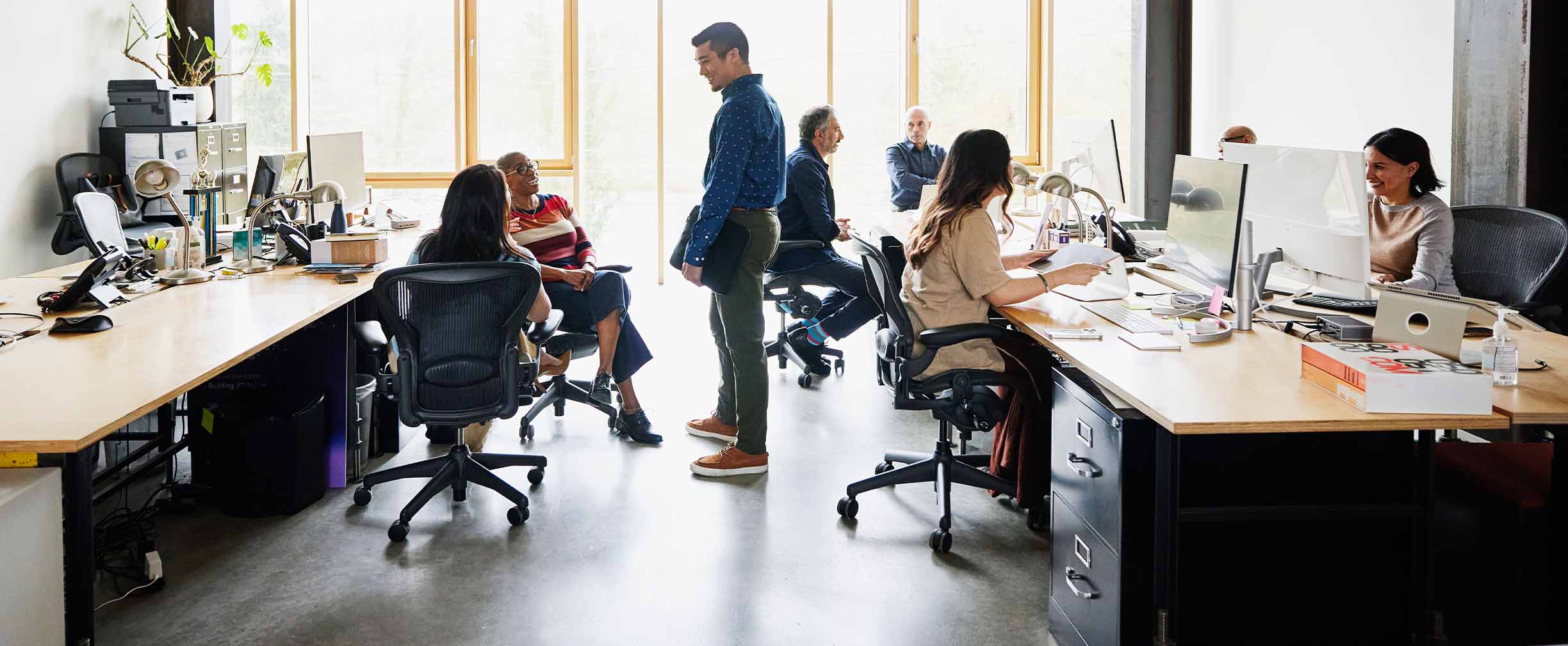 A group of diverse workers interact in a bustling open-concept office