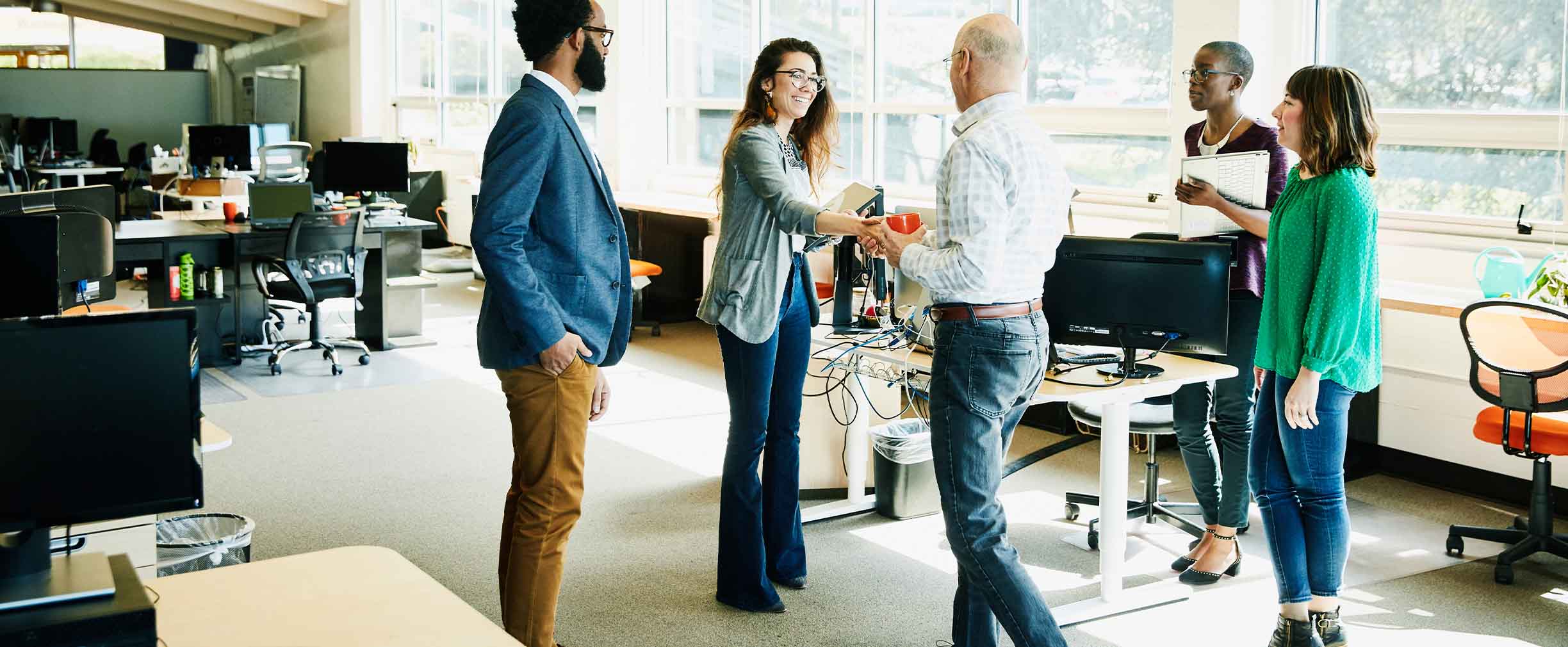 A group of diverse business owners meet in an open office and shake hands