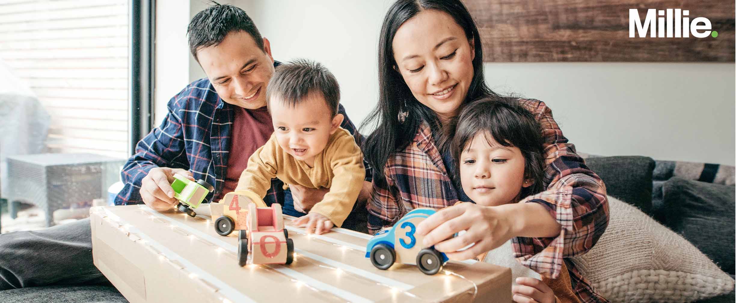 A mom and dad with their two young children playing with toy cars in their living room.
